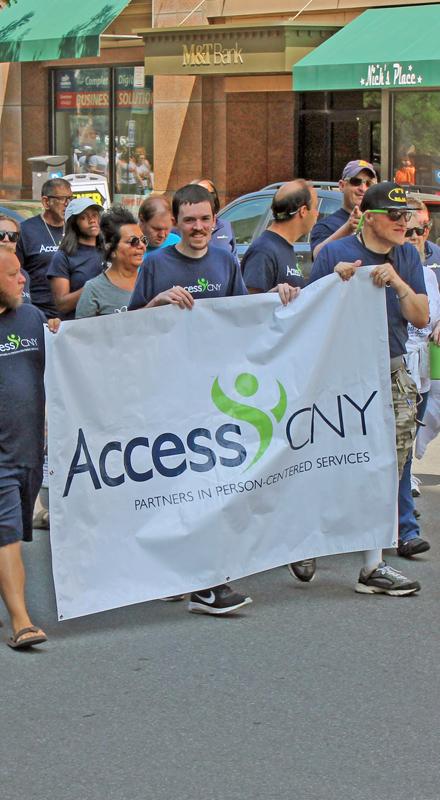A group of people in AccessCNY shirts march with a large AccessCNY banner