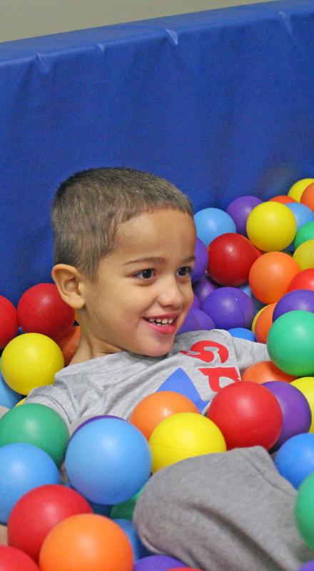 A young boy lays in a ball pit with multicolored balls