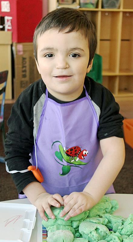 young boy plays with play doh on a table