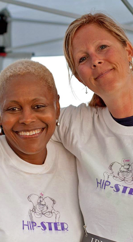 Two women in white and purple shirts smile at the camera