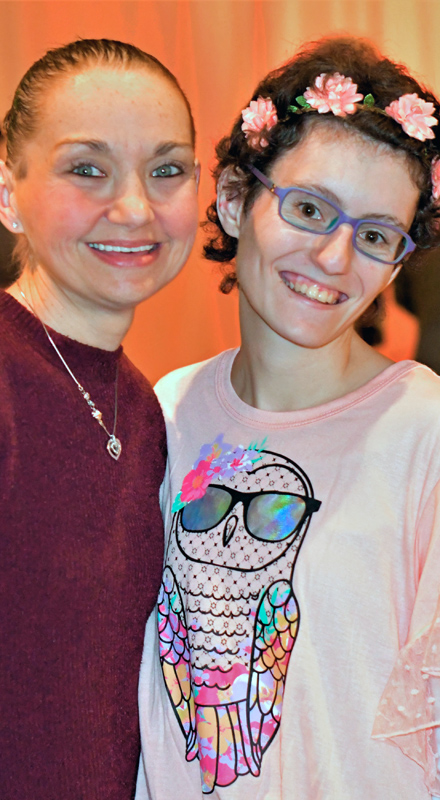 Two white women smile at the camera. One woman wears flowers in her hair.