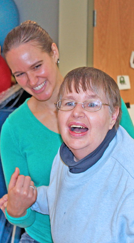 A young white physical therapist holds the hand/supports an older white woman.