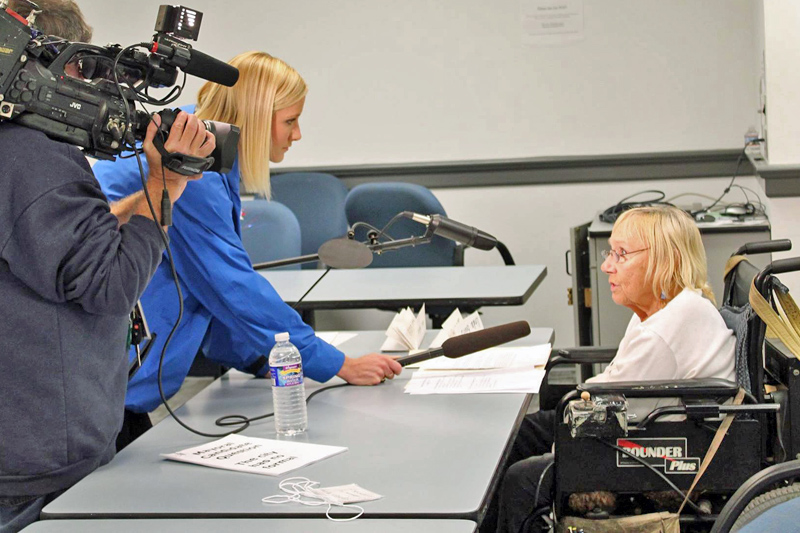 A reporter interviews Sally Johnston while a cameraman films