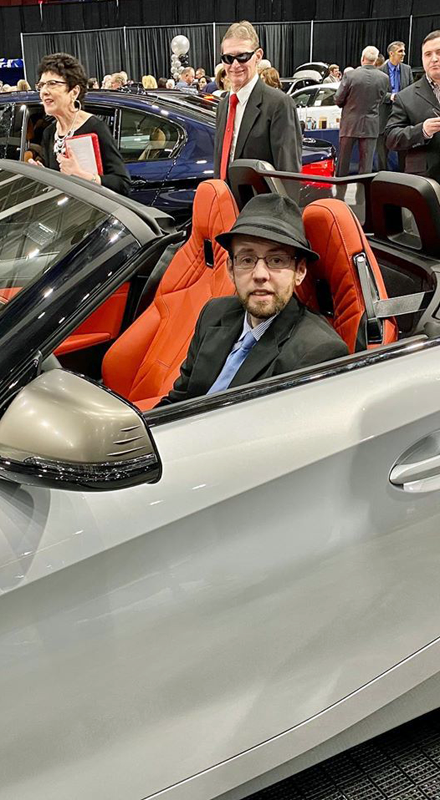 A white man in a hat sits in a car