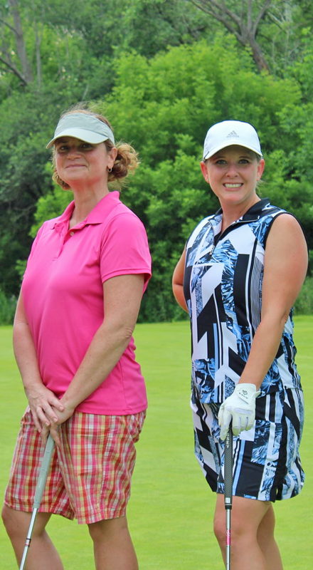 Two women in golf attire smiling and holding golf clubs