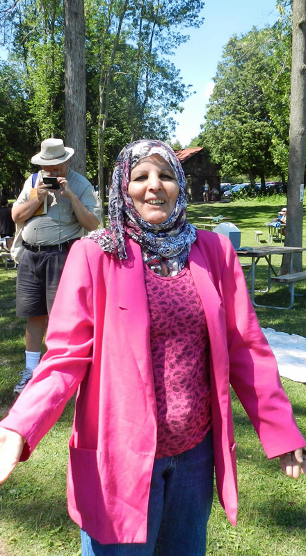 A woman in a pink coat and a head scarf smiles